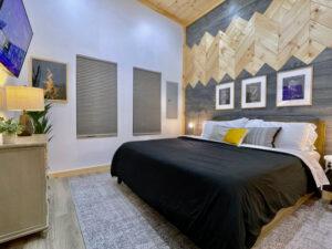 Cozy cabin bedroom in Red River Gorge featuring a king bed with black comforter, mountain-themed wood accent wall, and modern decor. Perfect for a relaxing getaway in Kentucky.