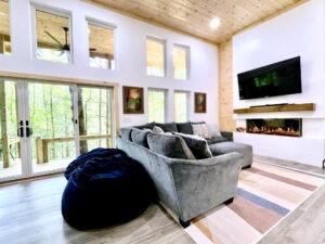 Cozy Red River Gorge cabin interior with a plush gray sectional sofa, a modern fireplace, and large windows showcasing the natural Kentucky landscape. A beanbag chair adds to the relaxed atmosphere of this inviting places to stay.