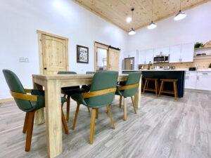 Cabin dining area in Red River Gorge rental. Rustic wood table with green chairs, modern kitchen with white cabinets, and wood accents create a cozy yet stylish space.