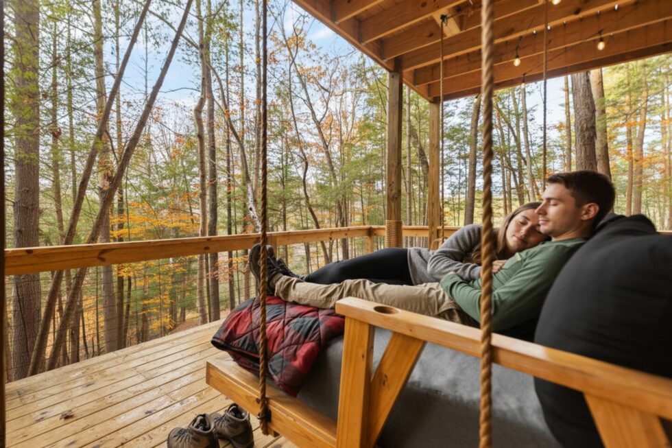 Couple relaxing on a porch swing at a Red River Gorge cabin rental. They're nestled under a blanket enjoying the wooded view from their cozy cabin.
