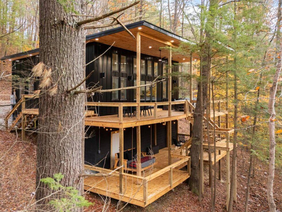 Trickle Creek Retreat, a modern cabin rental in Red River Gorge, KY, features a multi-level deck nestled among trees. Black siding contrasts with the natural wood of the decks, creating a cozy, elevated getaway.