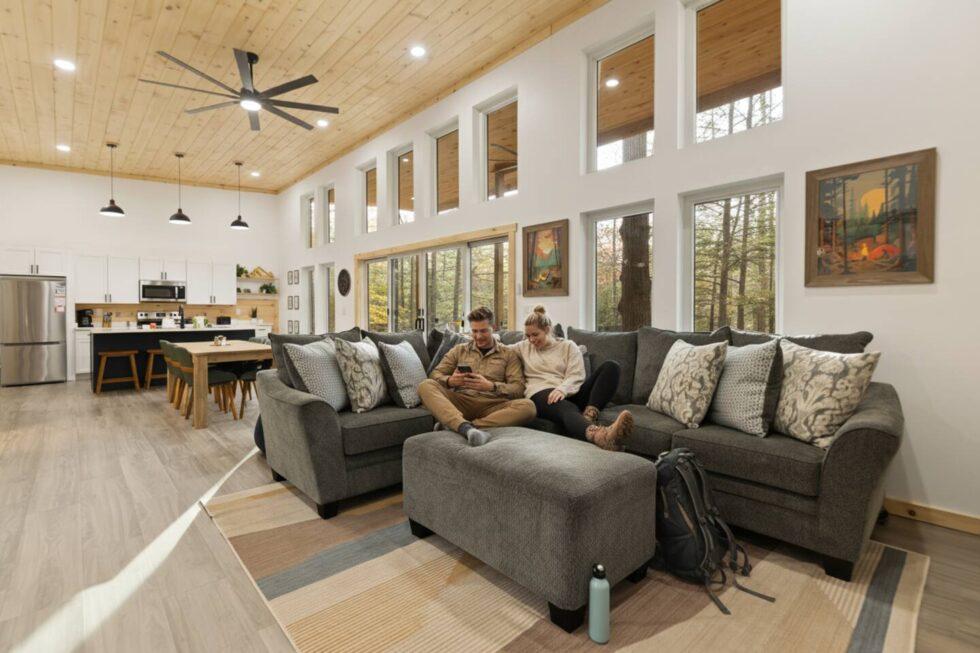 Couple relaxing in the living area of a Red River Gorge cabin rental. Natural light floods the open-concept space with a modern kitchen and cozy seating. Perfect for a Trickle Creek Retreat vacation.