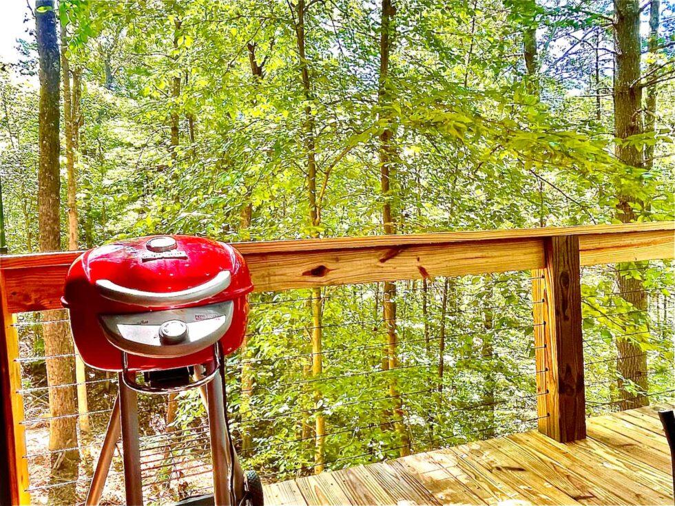 Red grill on a cabin deck at Red River Gorge. The wooden deck overlooks a lush green forest, perfect for grilling during a cabin rental getaway.