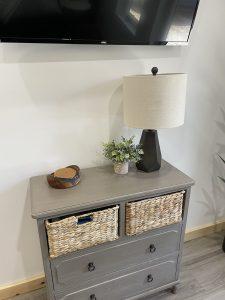 Gray dresser with baskets, lamp, and decor on top.