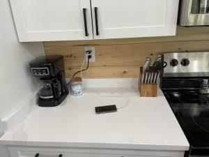 Kitchen counter with coffee maker, knife block, stove, and phone charging.