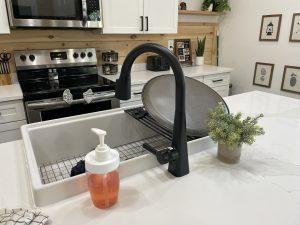 Kitchen sink with drying rack, faucet, soap, and dish. White cabinets above.