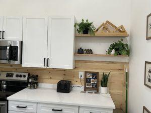 Kitchen with white cabinets, wood paneling, floating shelves with plants and decor.
