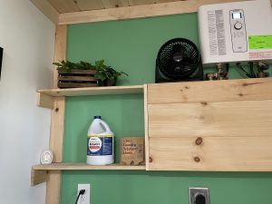 Laundry room shelf with bleach, detergent sheets, fan, and on-demand water heater.